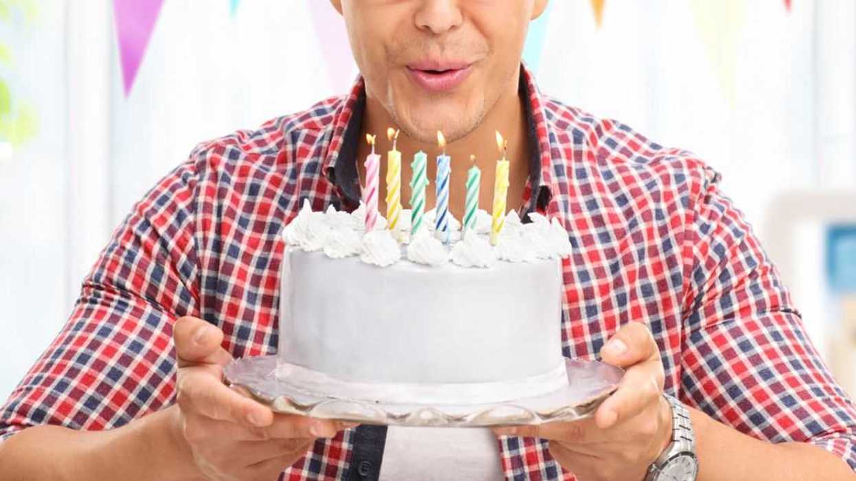 Joyful young man blowing candles on a birthday cake and looking into the camera at home.