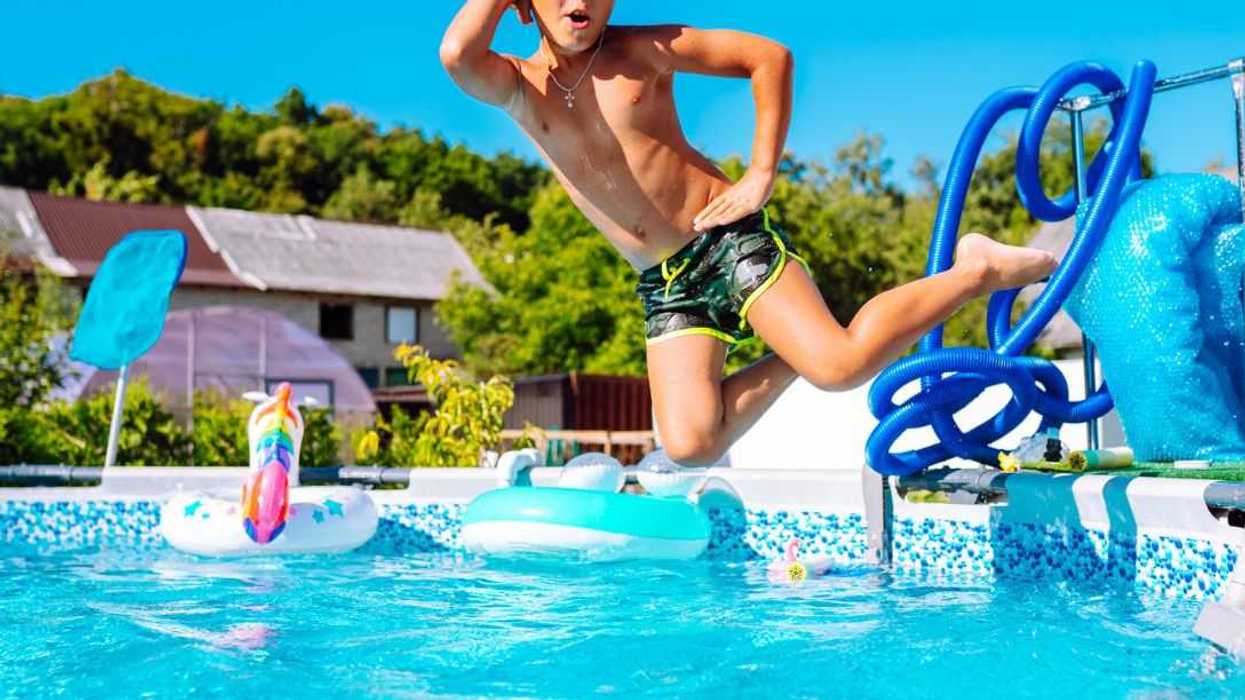 Little boy in swimming goggles and trunks diving into a swimming pool while looking at camera in humorous model pose on a sunny day.