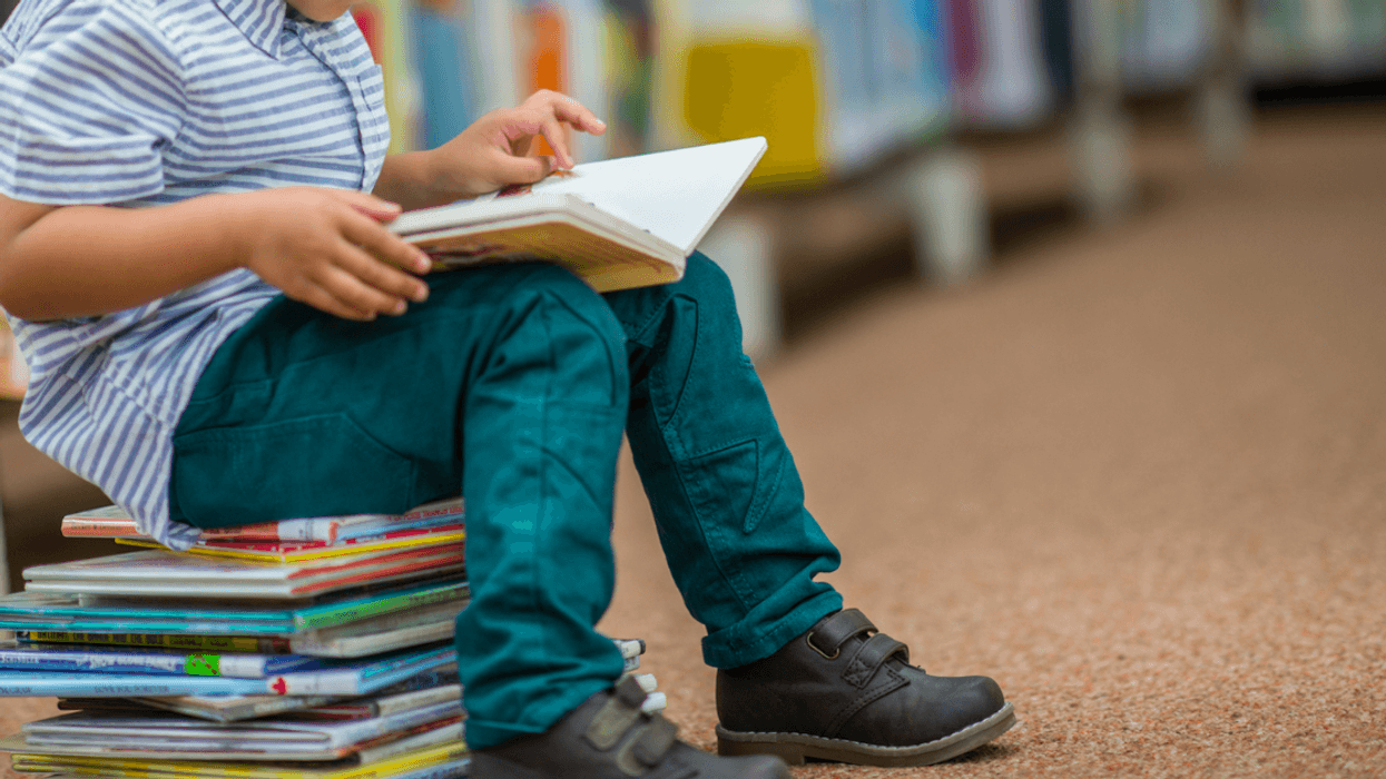 Little boy sitting on a pile of books and reading a book.