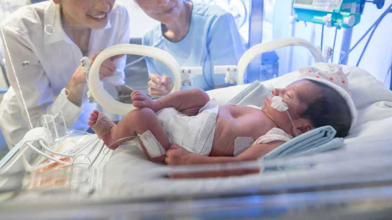 Loving mother and nurse at neonatal intensive care unit looking tenderly at the newborn baby in an incubator with oxygen.