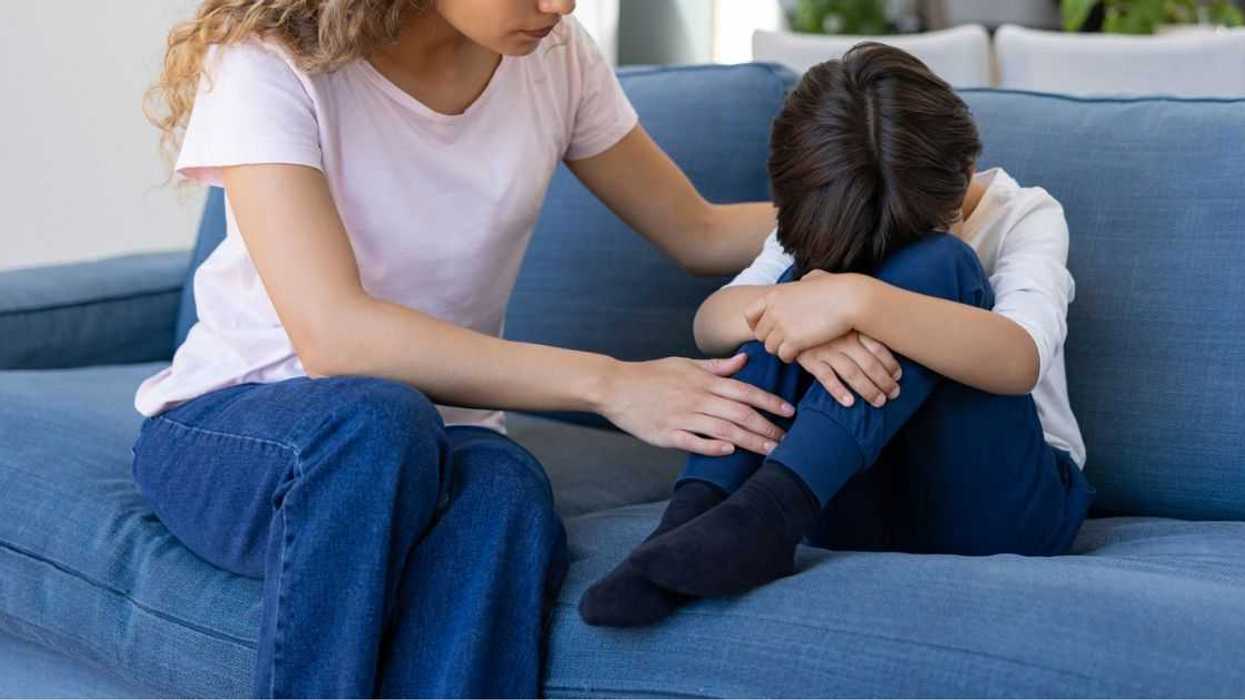Loving mother trying to calm down her sad son while he is crying at home on the couch.