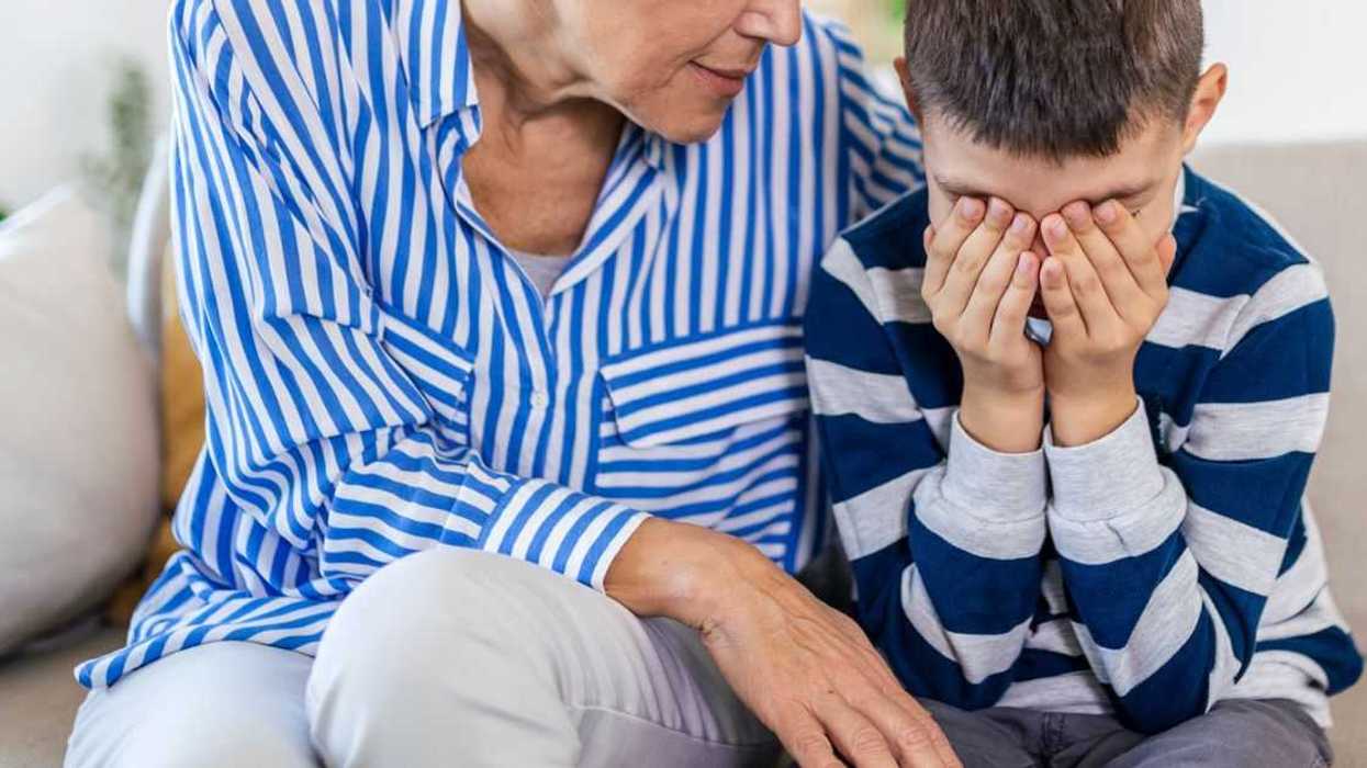 Loving, understanding grandma embracing little crying boy while sitting on couch.