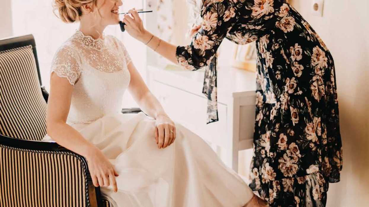 Make-up artist applying lipstick on excited bride during wedding.