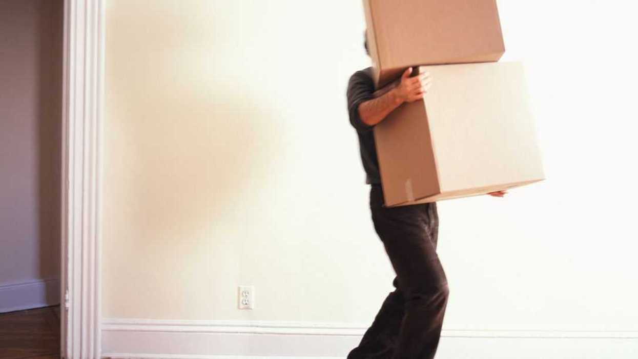 Man carrying moving boxes in to a bare room.