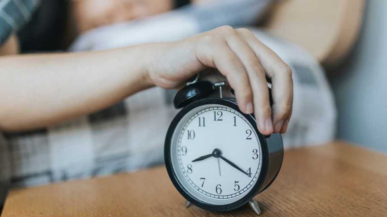 Man in bed reaching for alarm clock.
