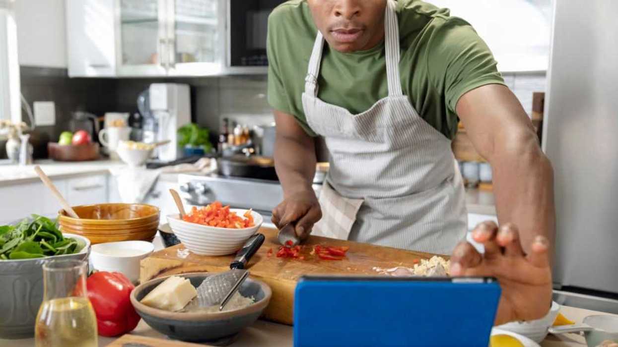 Man in his 20s making lunch, cutting bell peppers, using digital tablet with online recipe in kitchen, enjoyment, connection, domestic life.