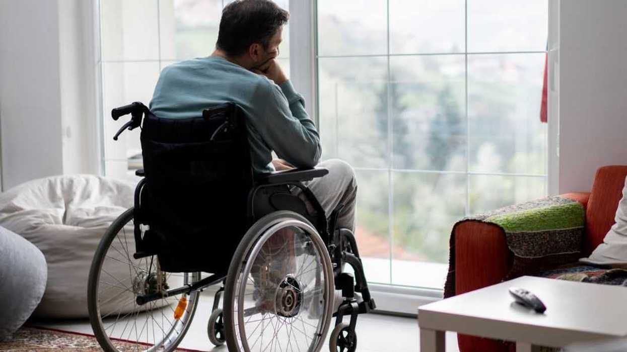 Man in wheelchair looking through large window reflecting in thought.