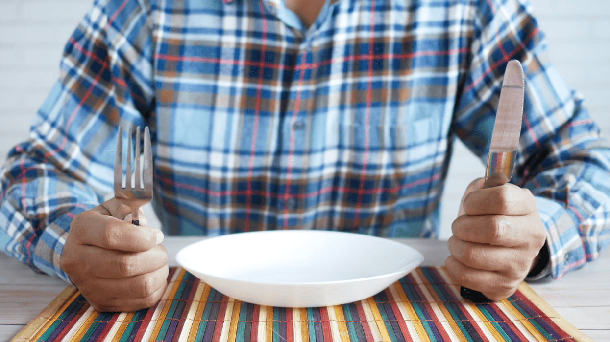 man seated at table holding knife and fork with empty bowl