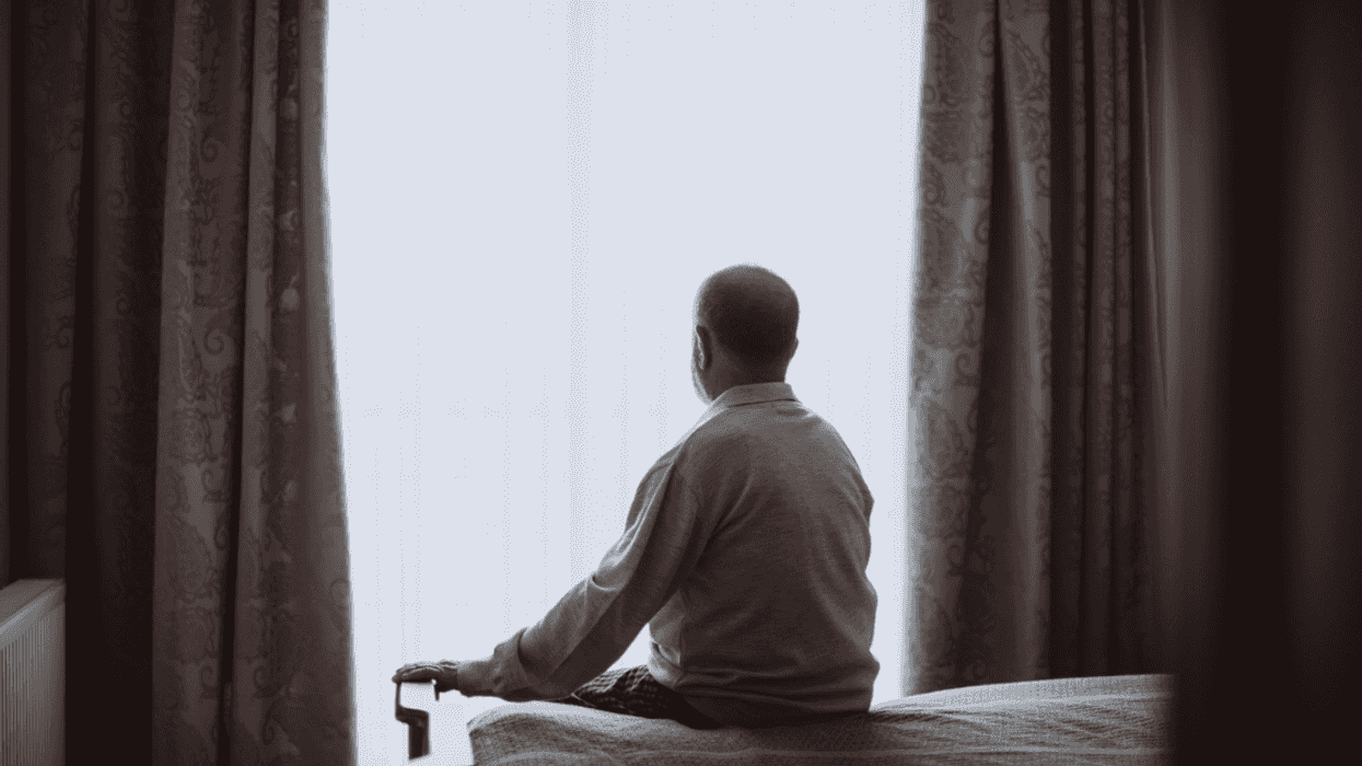 Man sitting on bed looking out window.