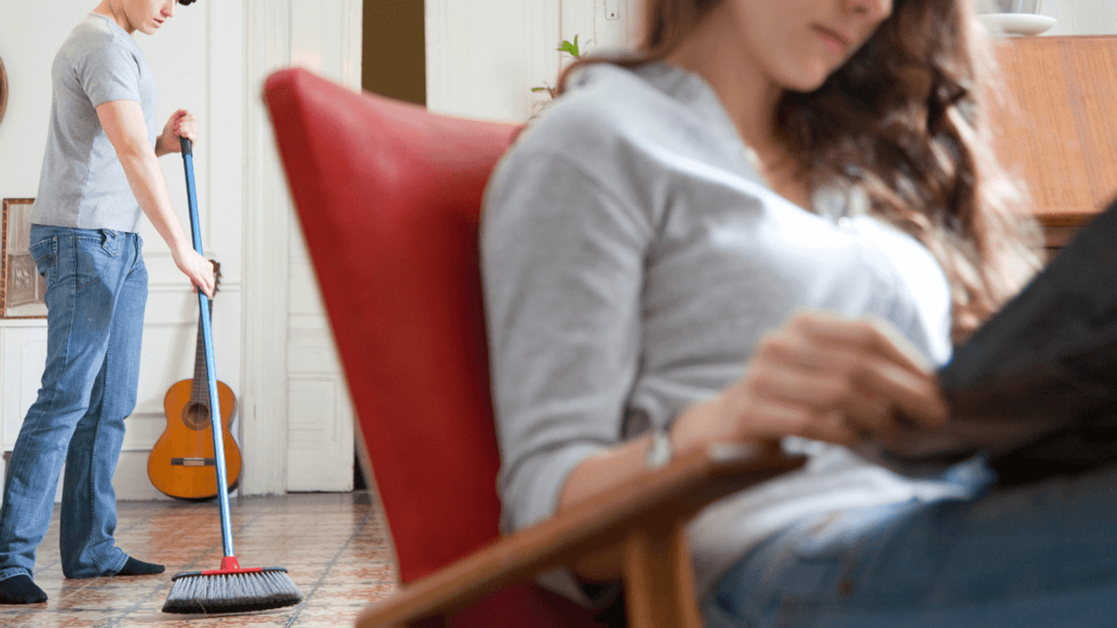 man sweeping in background as woman sits reading