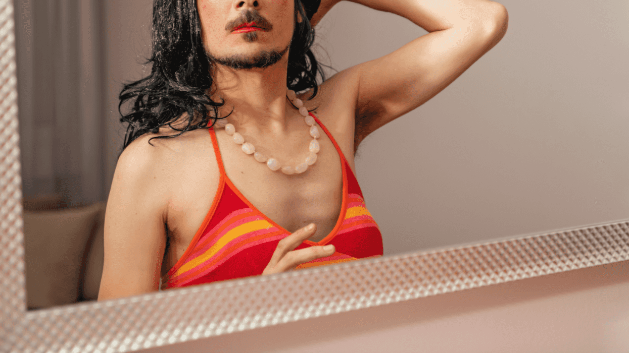 Man wearing a dress looking in the mirror and striking a pose.