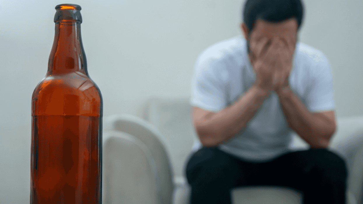 man with head in hands with bottle of alcohol in foreground