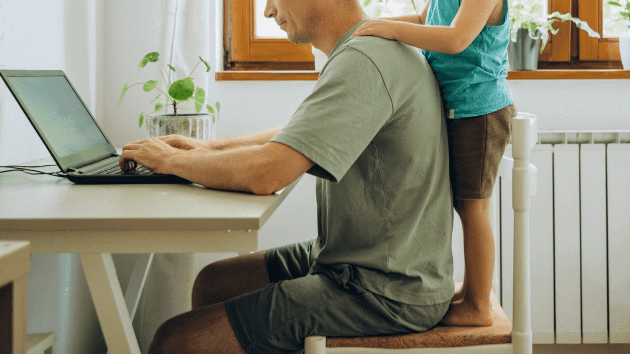 man working on laptop with child standing behind him