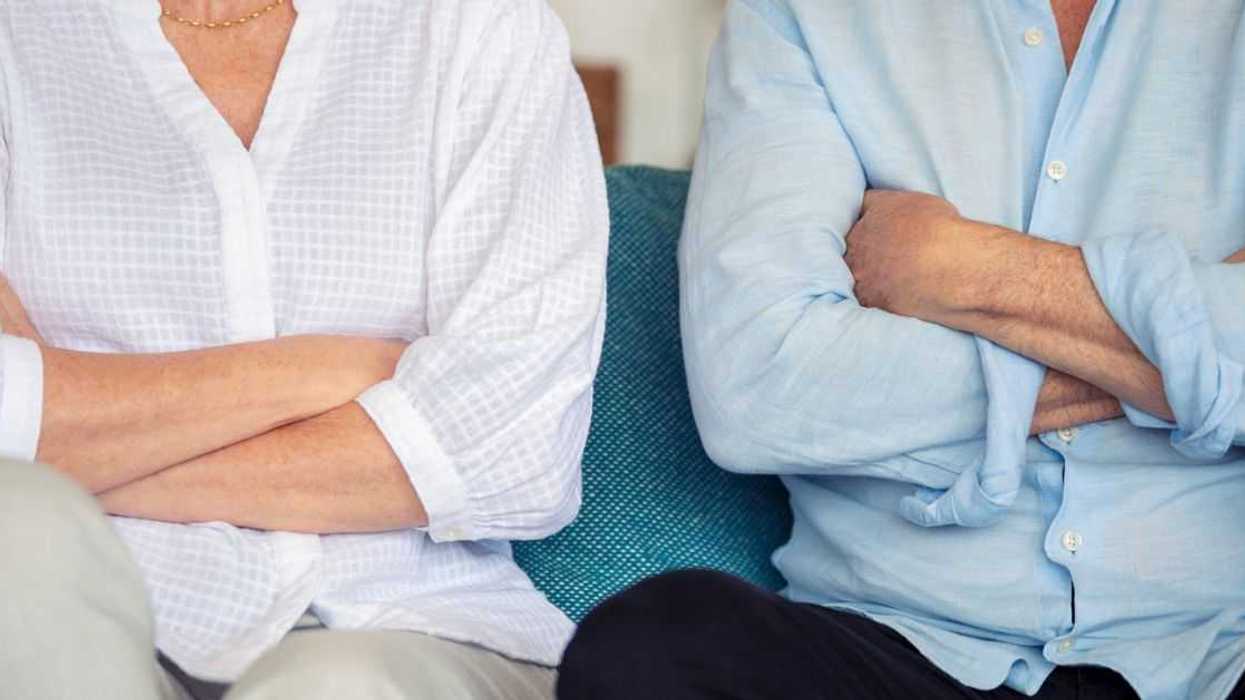 Mature couple fighting at home sitting on the sofa. They both have their arms crossed.