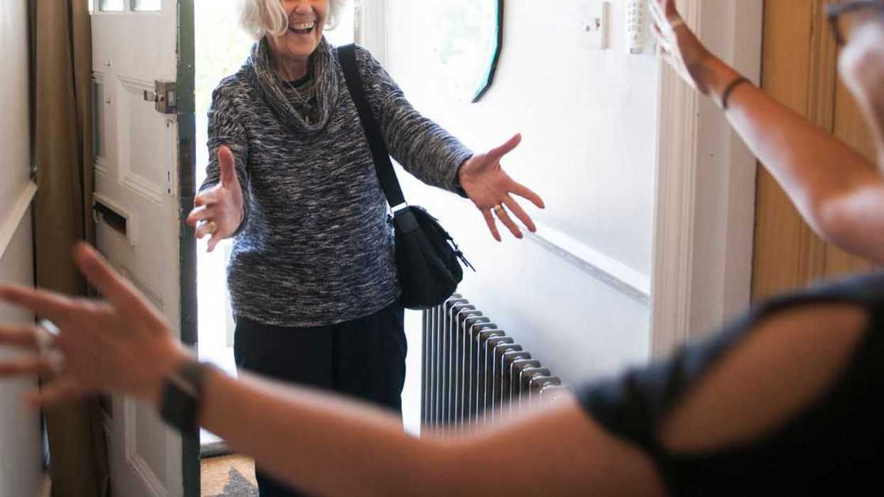Mature lady entering front door of house, holding out her arms to hug another woman.