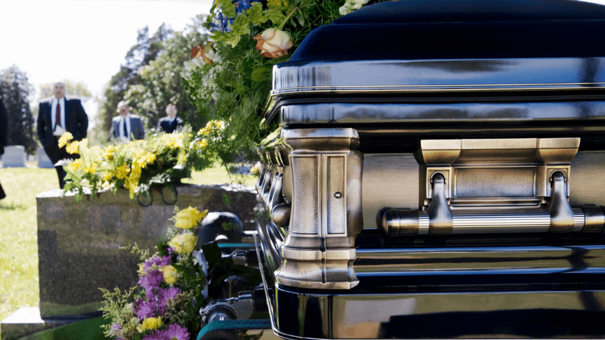 men in suits in cemetery with casket in foreground