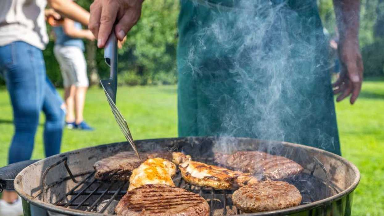 Mid section of man turning burgers and meat on barbecue grill in garden.