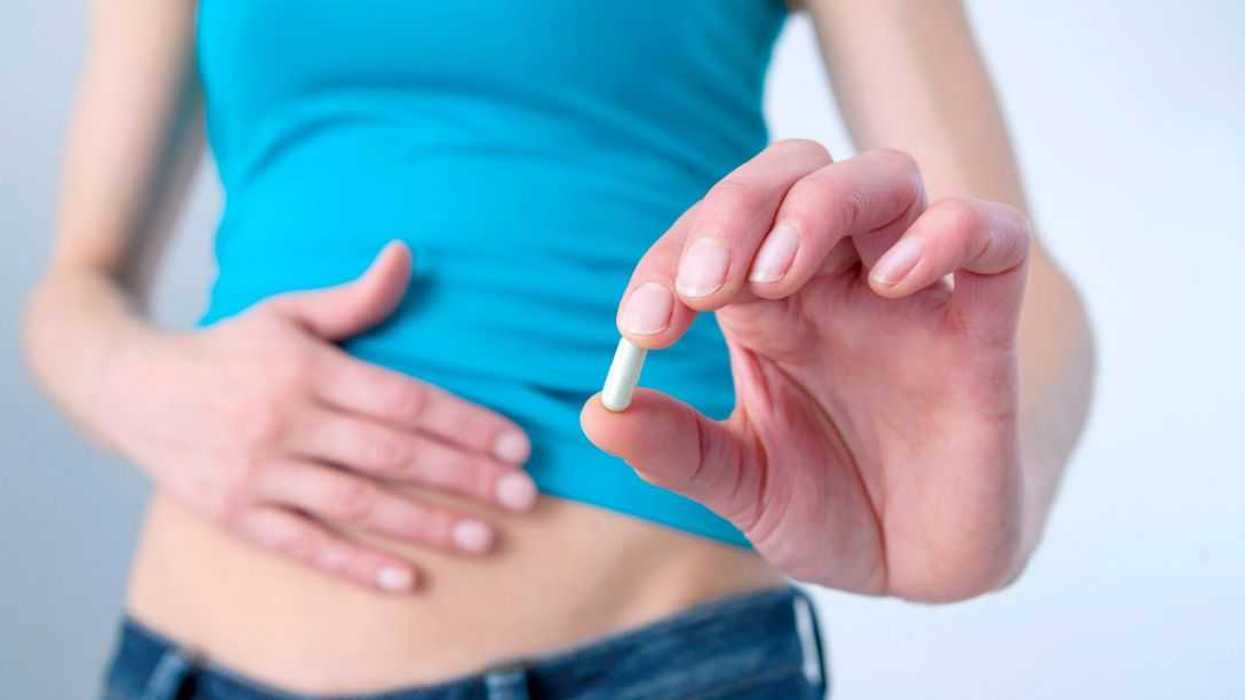 Mid-section shot of a young woman patting her stomach and holding up a pill.