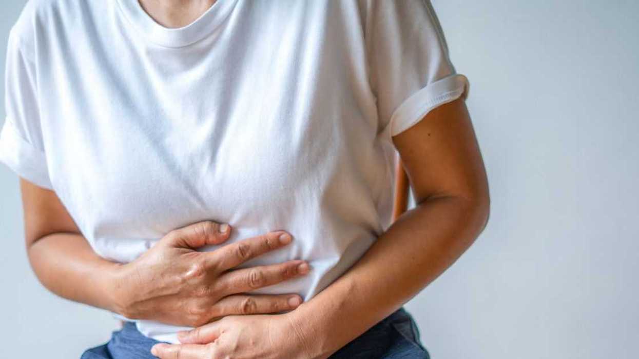 Mid-shot of a woman holding her stomach, crippled by pain.