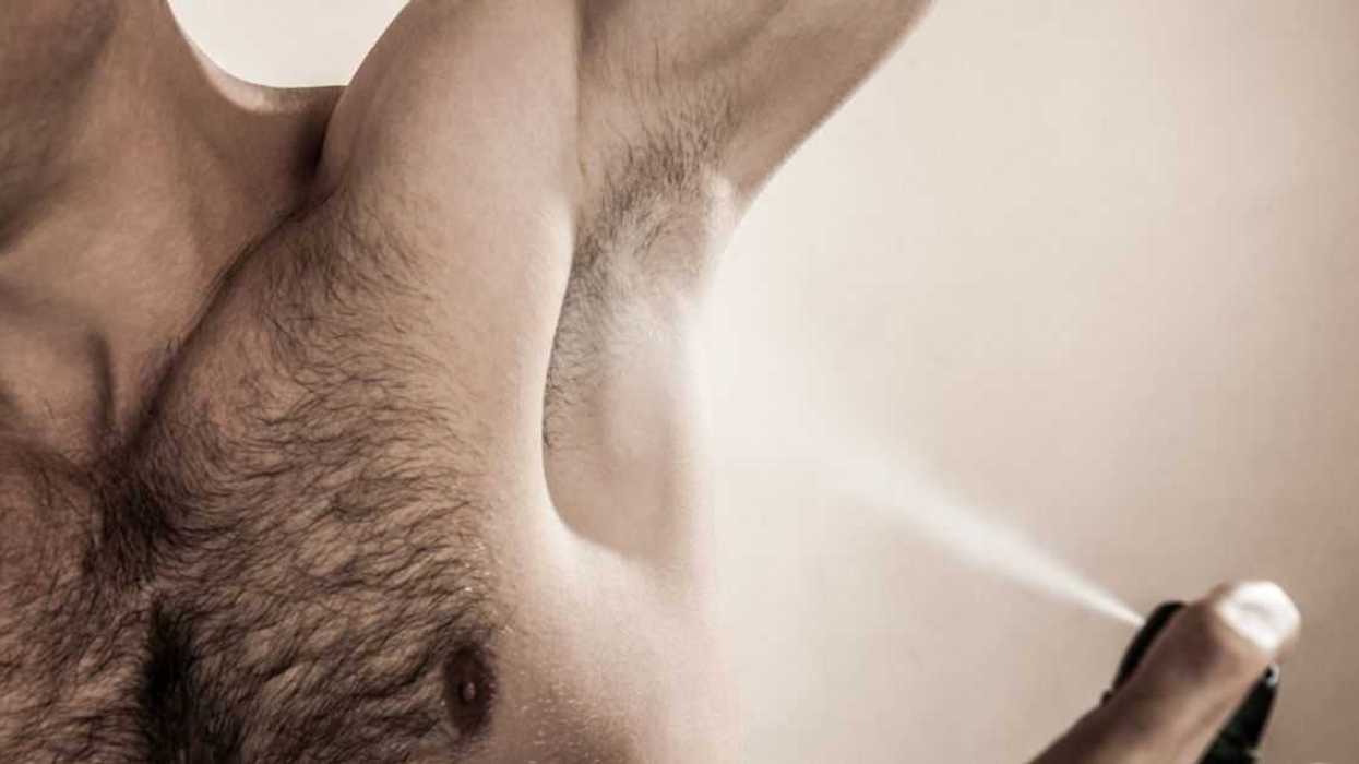 Mid studio shot of an adult man spraying deodorant.