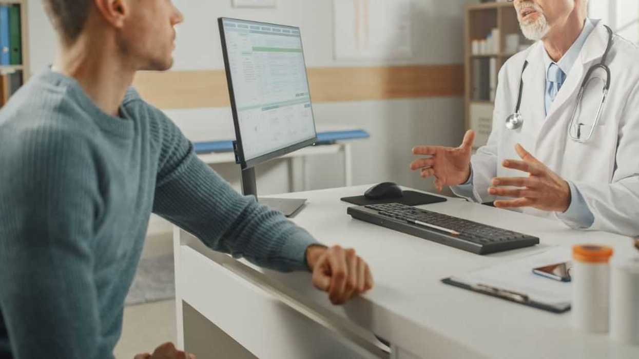 Middle Aged Family Doctor is Talking with Young Male Patient During Consultation in a Health Clinic.