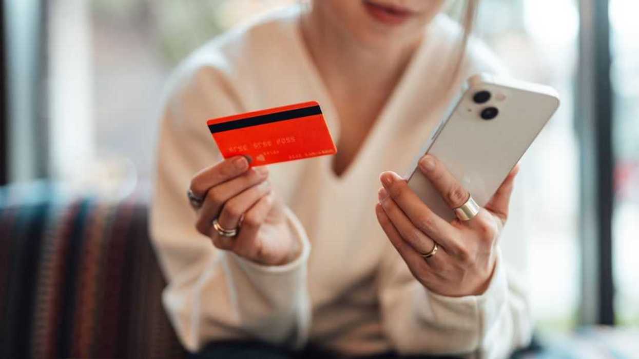 Midsection of a young woman holding a credit card while using smartphone, sitting on sofa. Online shopping and electronic payment.