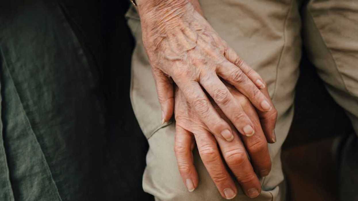 Midsection of retired senior couple holding hands sitting at a nursing home .