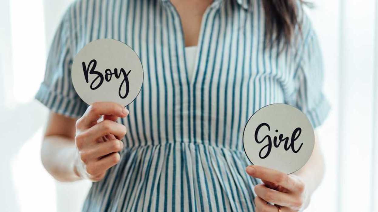 Midsection shot of a pregnant woman holding two cards showing different genders, predicting the sex of her baby. Baby shower game ideas.