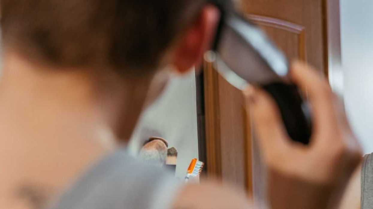 Mirror reflection of short haired woman in tank top using haircutting machine