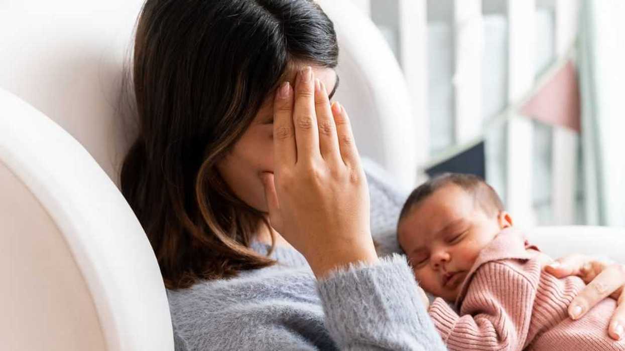 Mother sitting on couch in nursery feeling postpartum depression with baby in her arms.