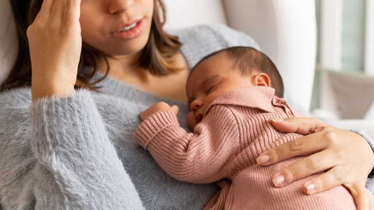 Mother sitting on couch in nursery feeling postpartum depression with baby in her arms.