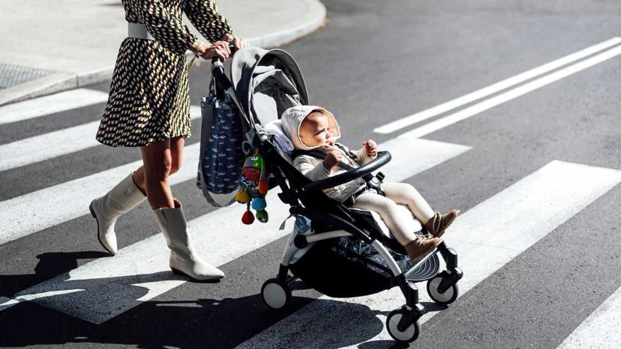 Mother with baby boy in carriage crossing the street in a city during a sunny day.