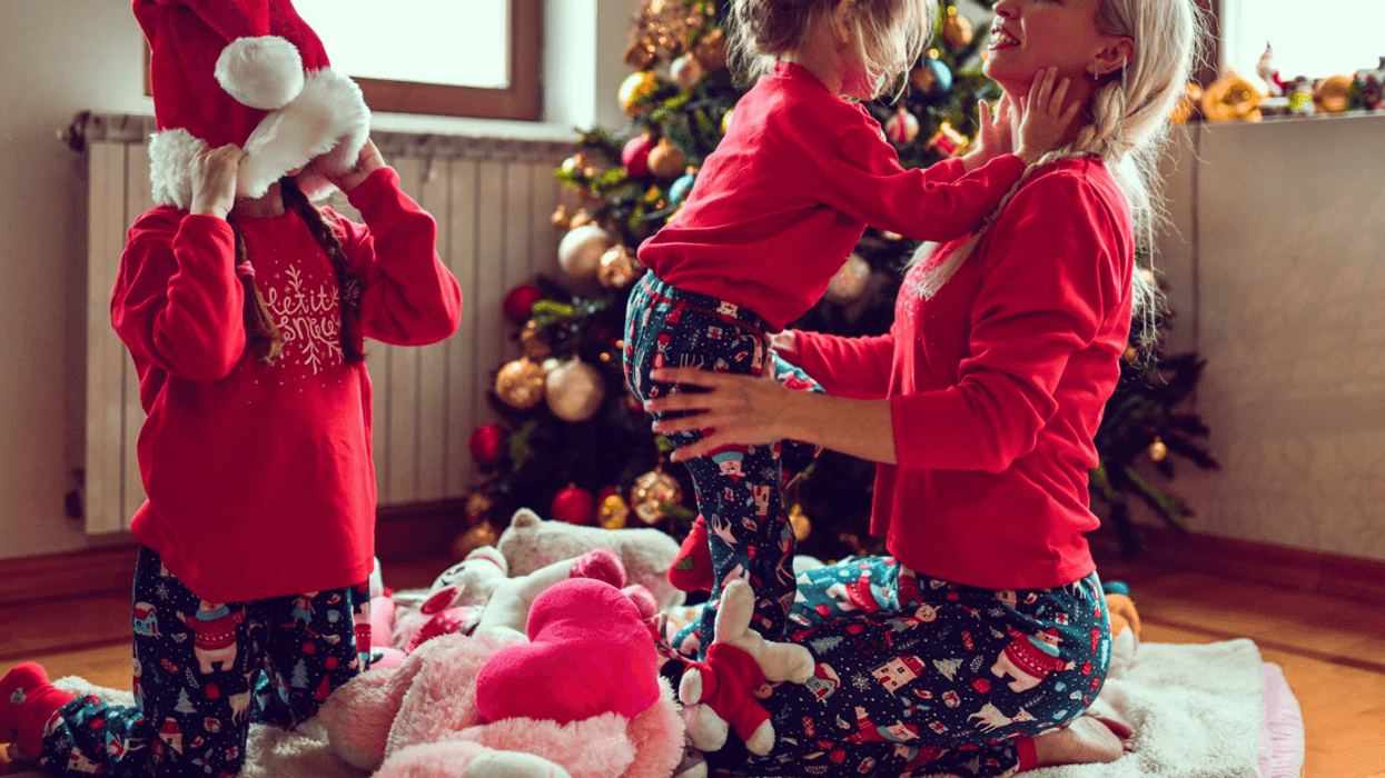 mother with two children in Christmas pajamas with toys in front of a tree