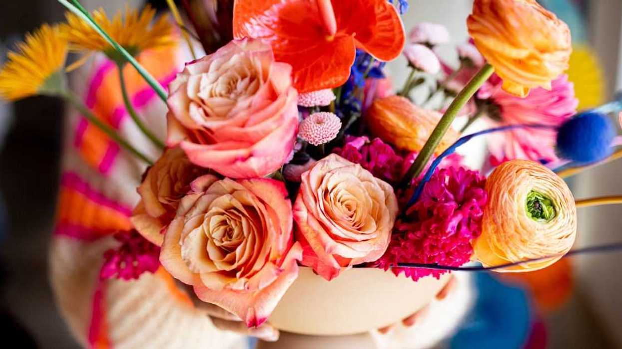Multi-colored flowers arranged in a vase being held by a woman.