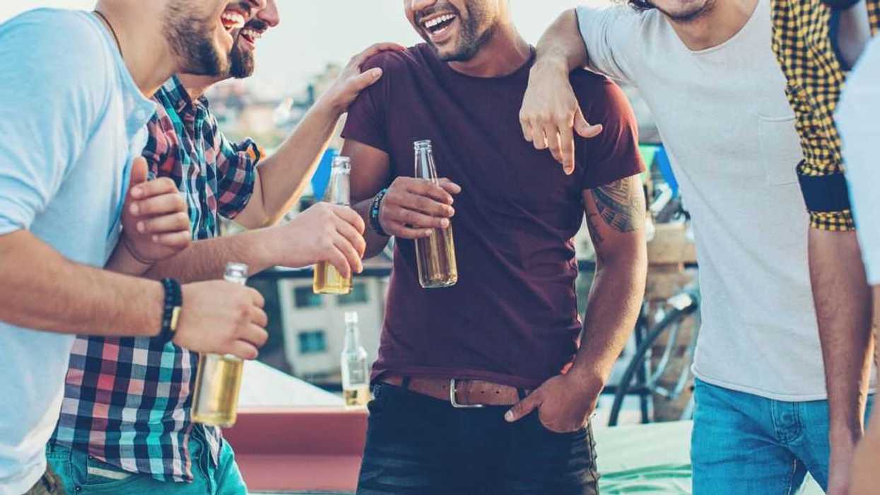 Multi-ethnic group of young men chatting and drinking beer on a rooftop party.