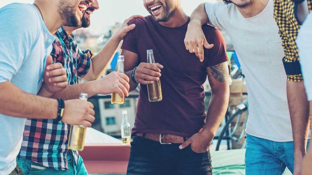 Multi-ethnic group of young men chatting and drinking beer on a rooftop party.