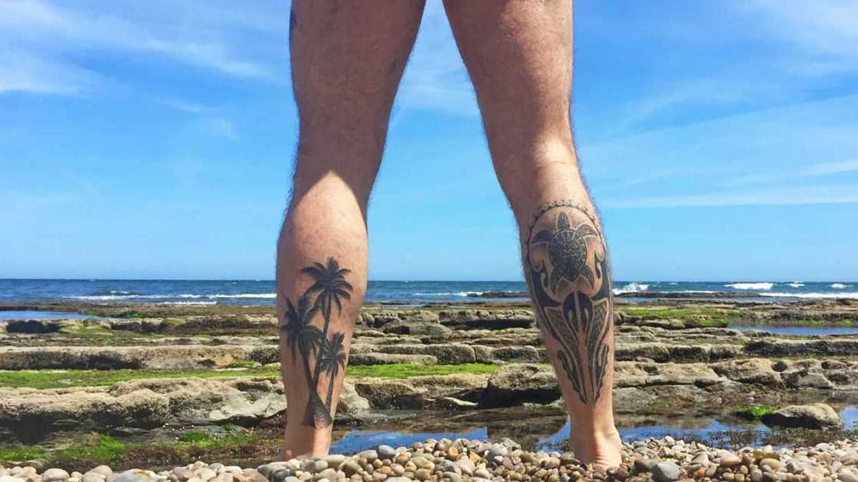 Naked man with tattooed legs looking at the sea on a beach