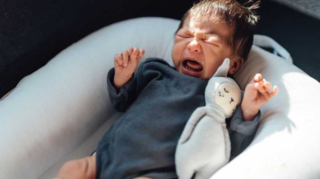 Newborn baby girl crying on bed.