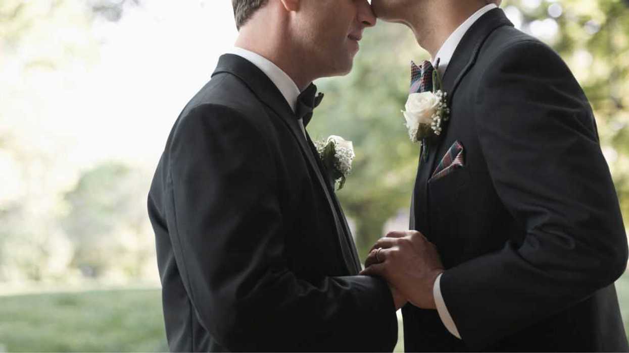Newlywed grooms kissing outside.