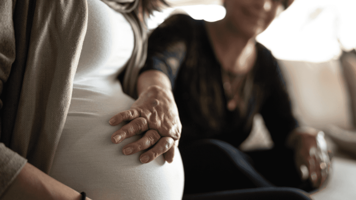 older woman with hand on woman's pregnant belly