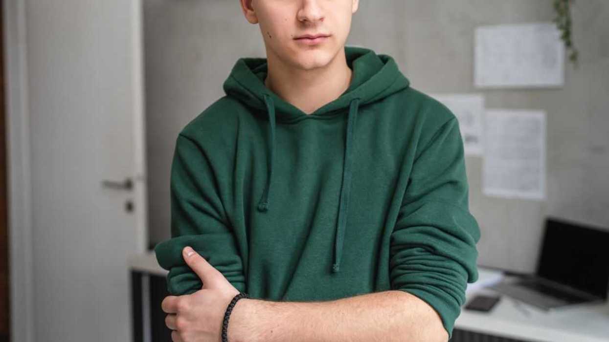 One teenage boy standing in a room at home wearing a green hoodie scene from the waist up.