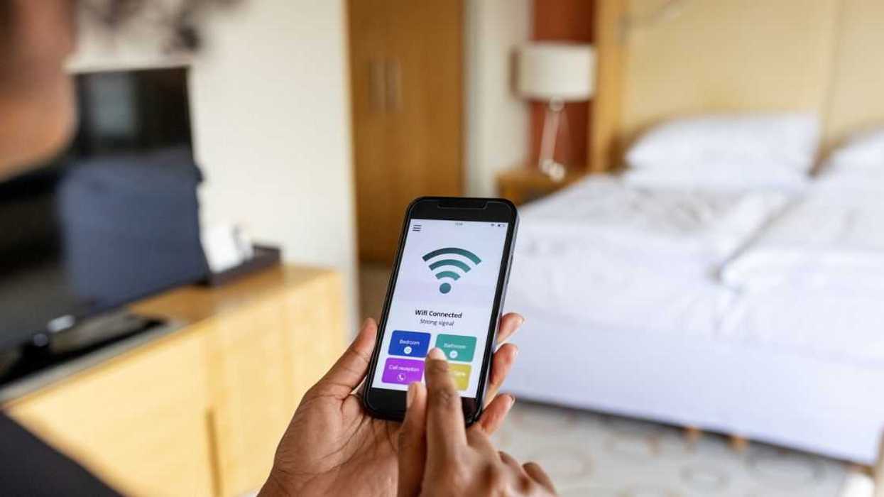 Over the shoulder view of a businesswoman connecting to the mobile wifi in a hotel room. Wifi icon on mobile phone display.