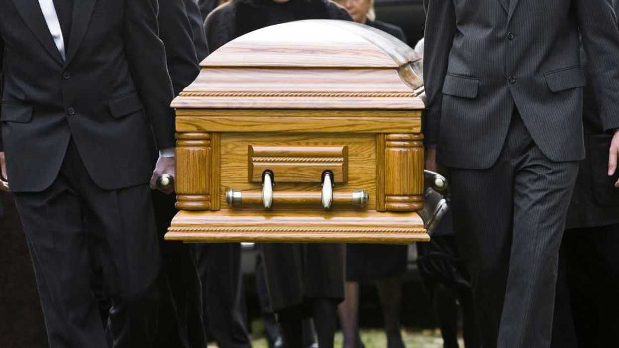 People carry a casket at an outdoor cemetary.