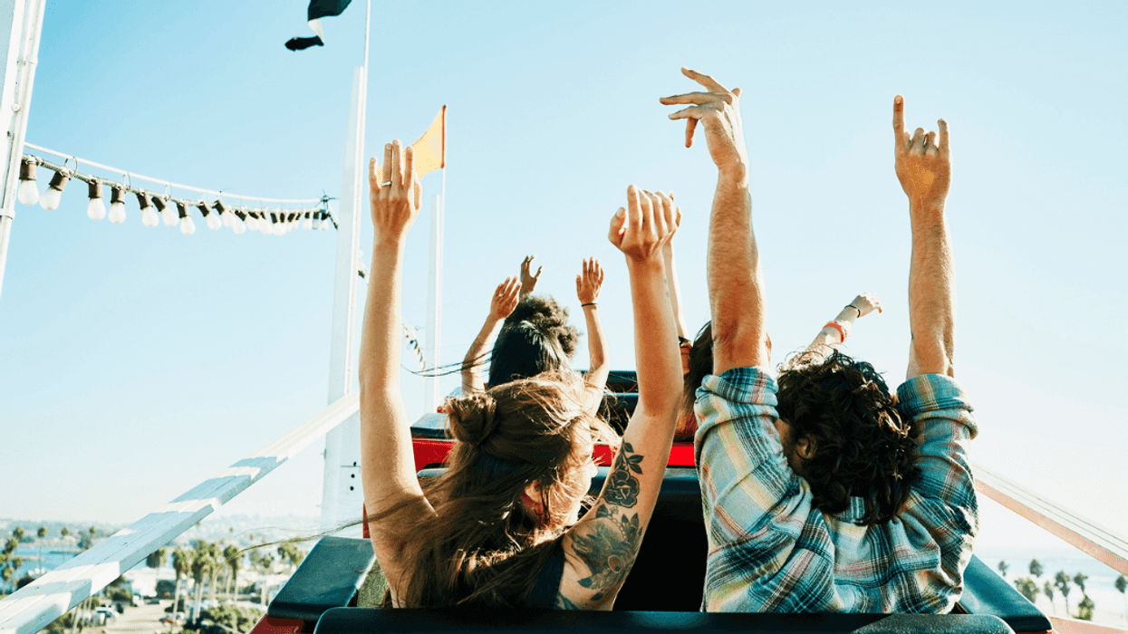 People holding their hands up on a roller coaster.