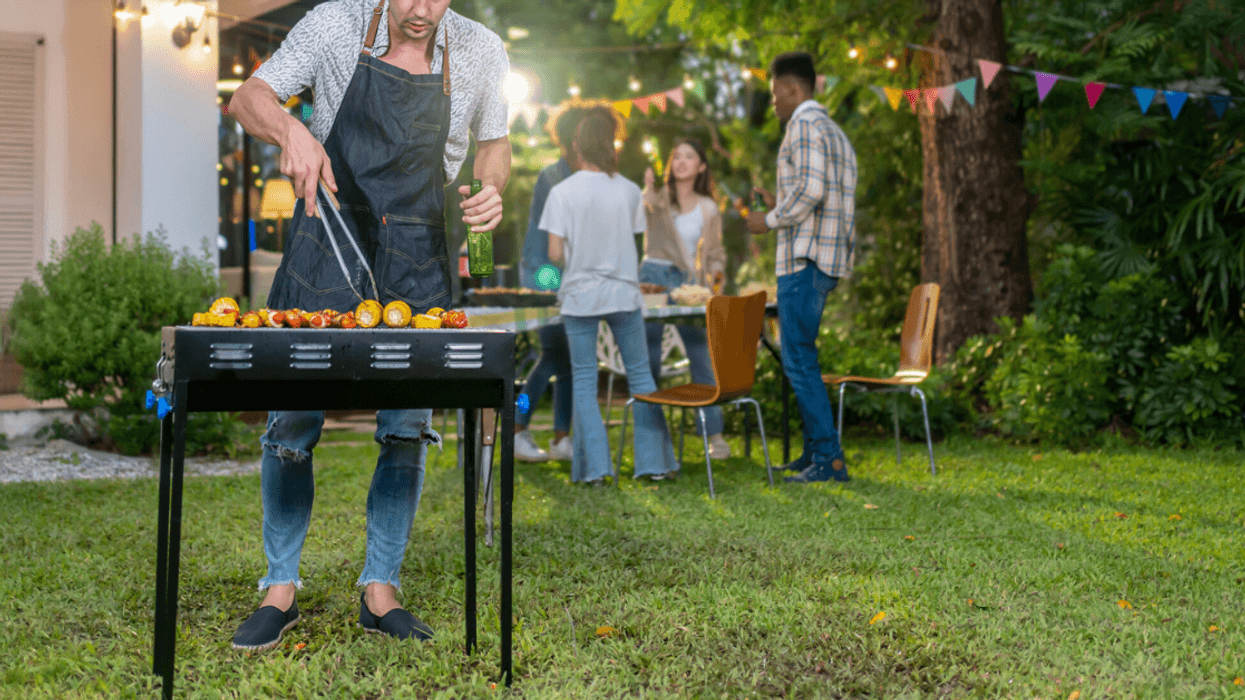 person cooking on a BBQ grill as people socialize in the background