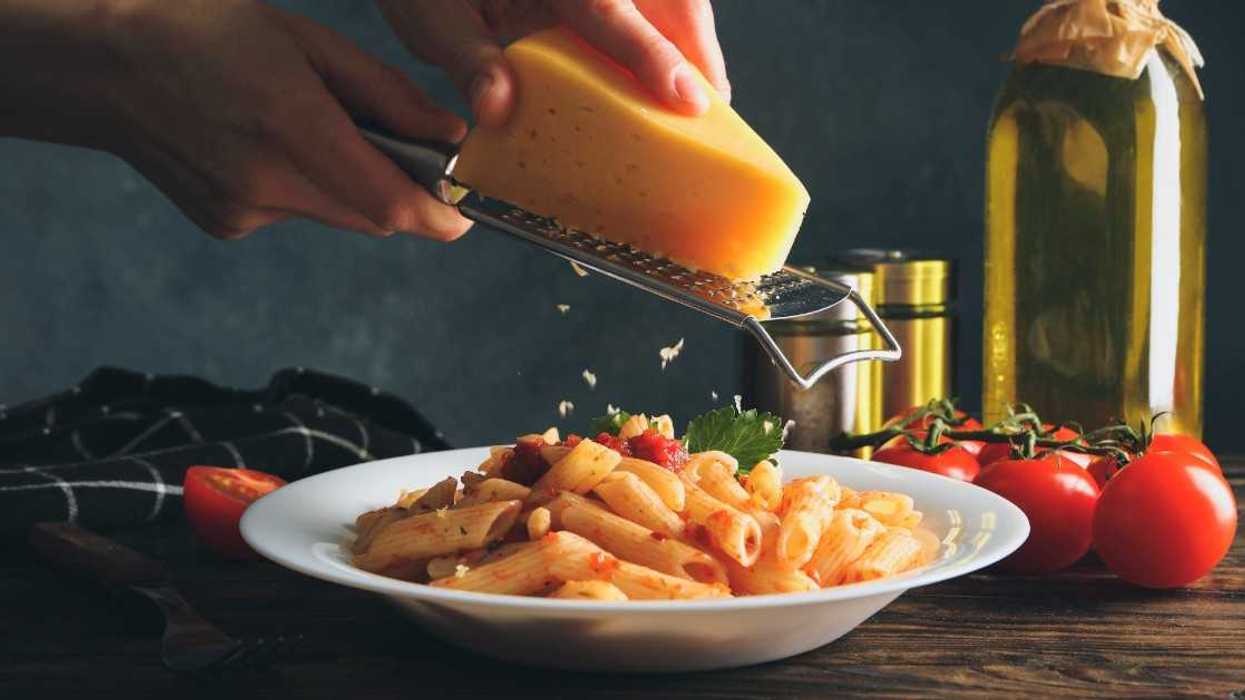 person grating cheese onto pasta