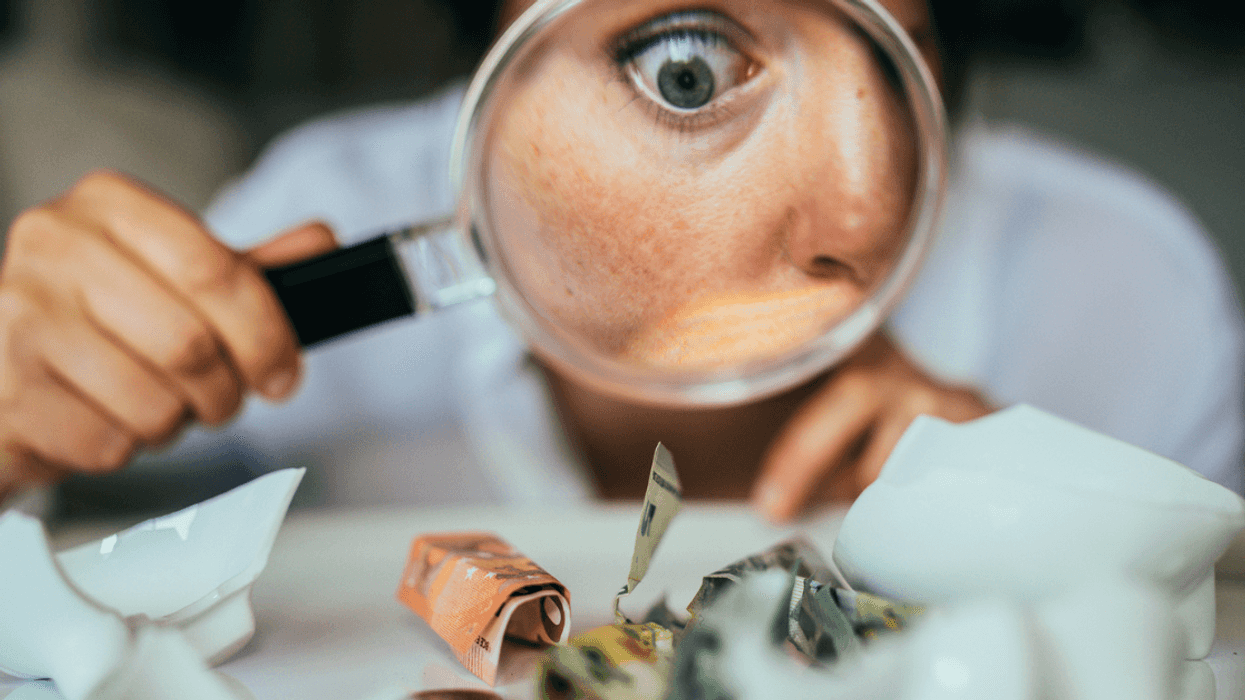 person looks at money from piggy bank with magnifying glass