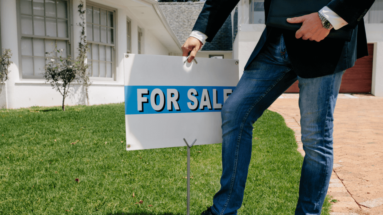 person putting "for sale" sign in front of house