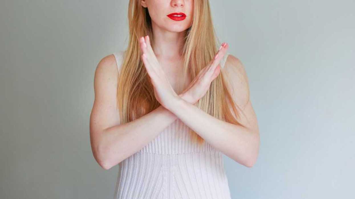 Photo of a pretty woman with her hands crossed as to show a 'no stop, forbidden' symbol on an isolated background.