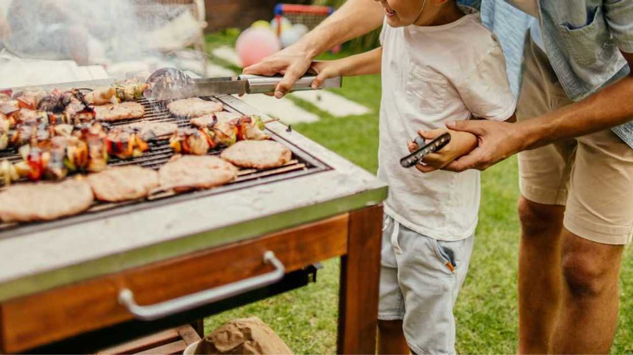 Photo of father and son grilling meat during a barbecue party in their yard.